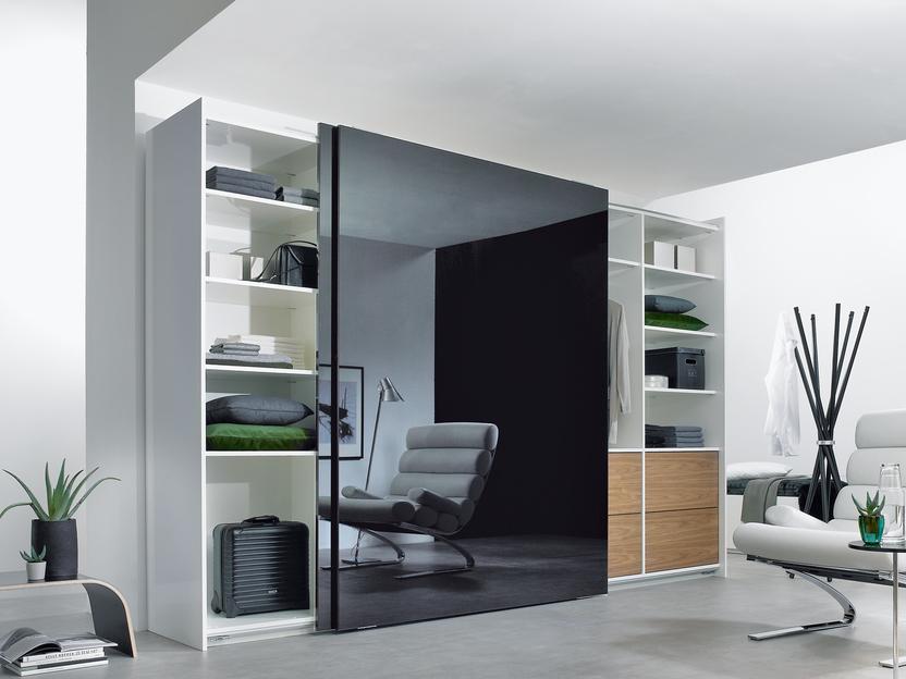 Wohnraumimpression mit abgetrennter Ruheoase Wohnraumimpression mit abgetrennter dunkler Glasschiebetür für Ruheoase und integrierten Einbauregalen