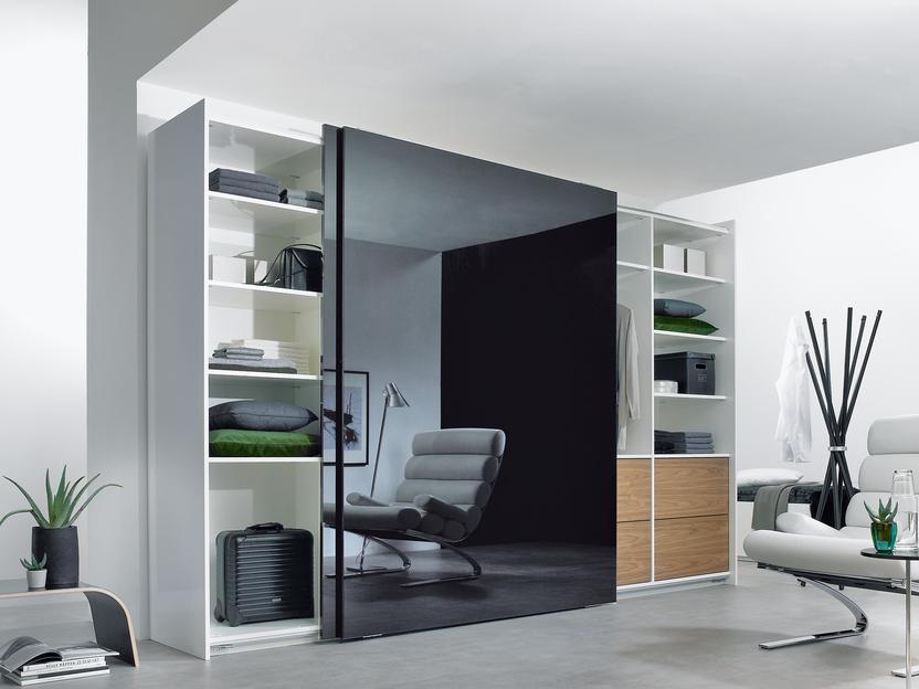 Wohnraumimpression mit abgetrennter dunkler Glasschiebetür für Ruheoase und integrierten Einbauregalen